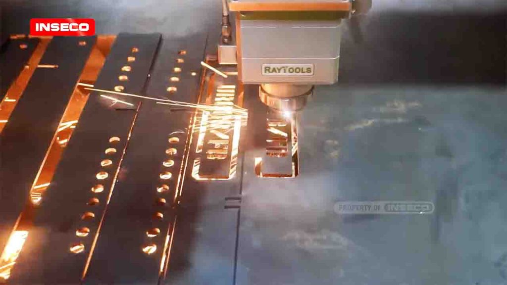 Mesin CNC laser cutting Raytools Inseco sedang memotong plat besi dengan sinar laser, tampak percikan api dan bentuk huruf pada material