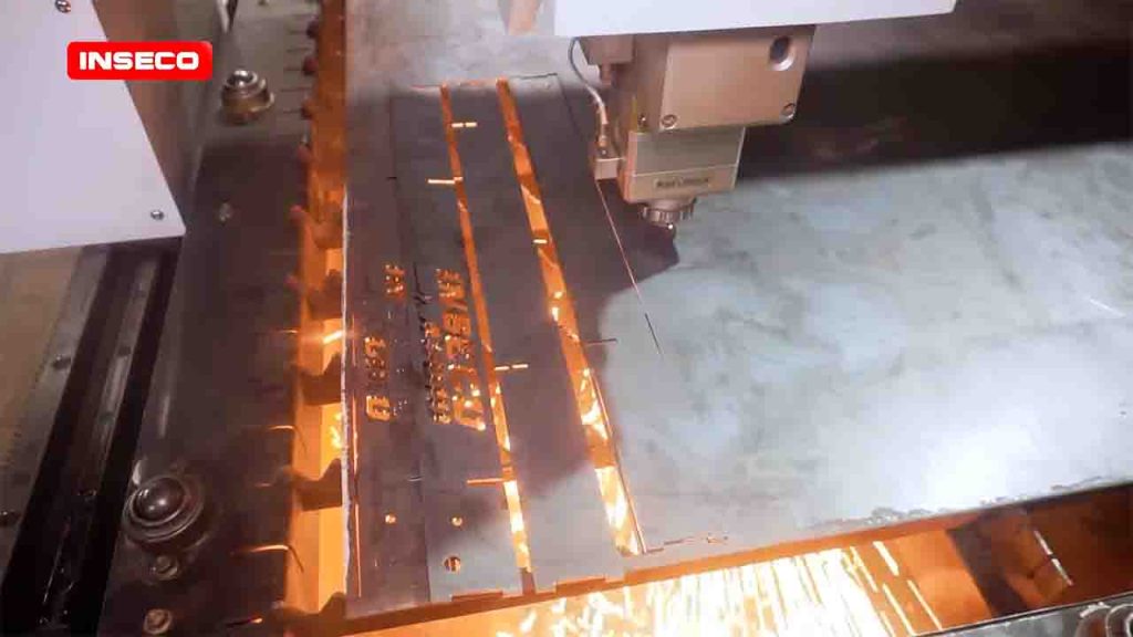 Mesin laser cutting CNC Inseco dengan kepala Raytools sedang memotong plat besi, menghasilkan percikan api terang dan ukiran tulisan pada material